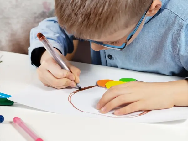 A child leaning over a piece of paper and drawing a picture with a marker